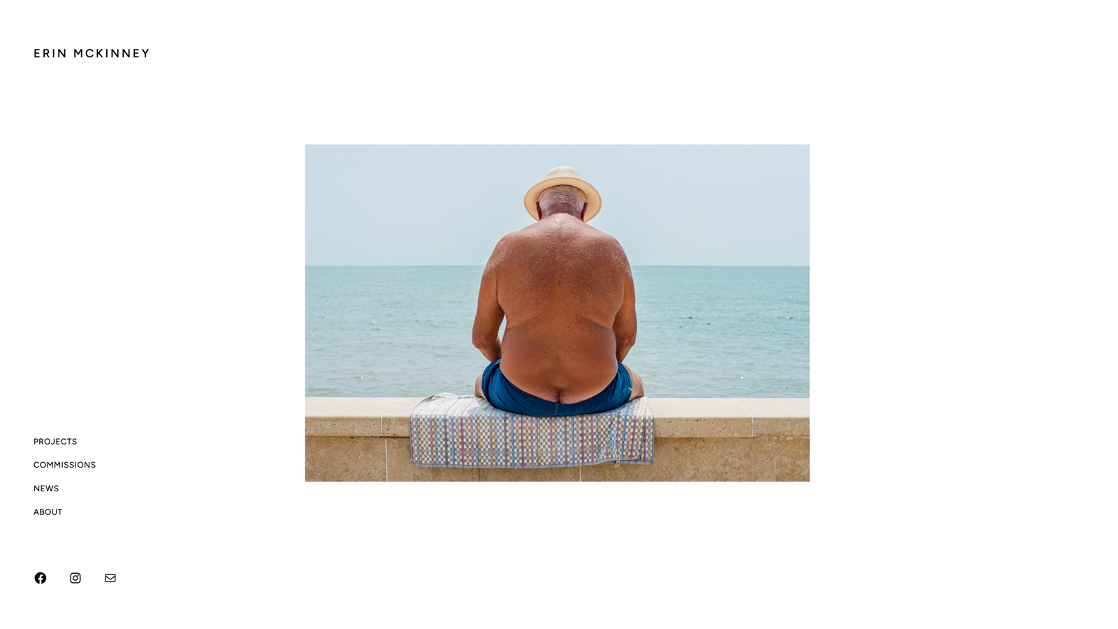 Minimalist portfolio homepage featuring a photograph of a man sitting by the sea, with navigation links along the left side.